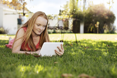 Grl with long red hair lying in grass with tablet - ZEF13929