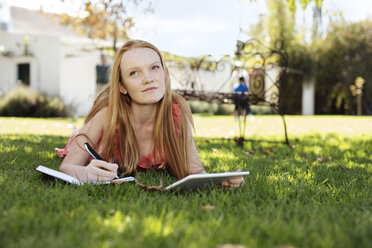 Grl with long red hair lying in grass with tablet and notebook - ZEF13931