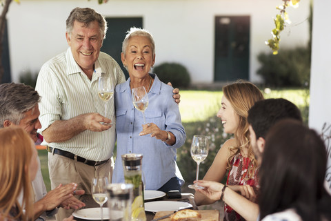 Glückliches älteres Paar mit Familie beim gemeinsamen Mittagessen im Freien, lizenzfreies Stockfoto