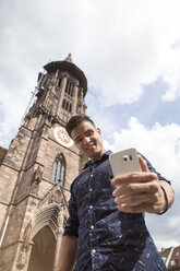 Deutschland, Freiburg, junger Mann macht ein Selfie vor dem Münster - MIDF00842