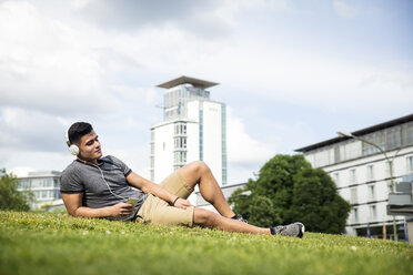 Young lying on meadow in urban park listening to music - MIDF00845