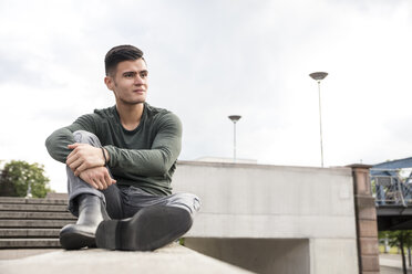 Junger Mann sitzt auf einer Mauer in der Stadt - MIDF00846