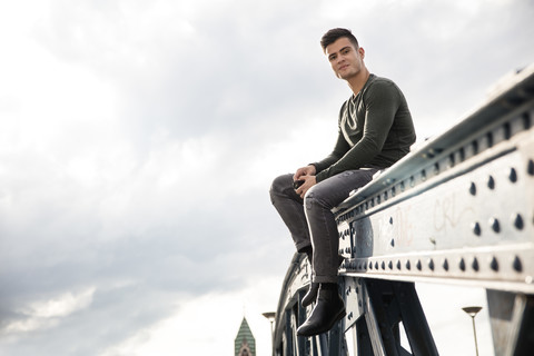 Young man sitting on railing of a bridge stock photo