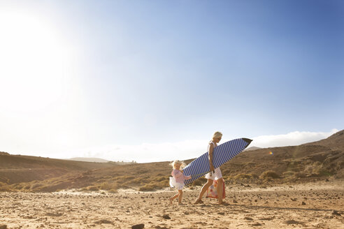 Spanien, Fuerteventura, Mutter und Tochter gehen mit Surfbrett am Strand spazieren - MFRF00857