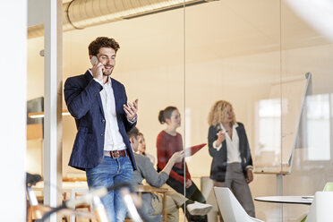 Businessman on cell phone in office with a meeting in background - PESF00652