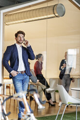 Businessman on cell phone in office with a meeting in background - PESF00653
