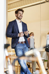 Smiling businessman with cell phone in office - PESF00655