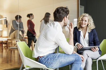 Zwei Kollegen unterhalten sich im Büro mit einer Besprechung im Hintergrund - PESF00661