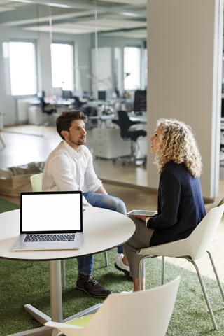 Two colleagues talking in office with laptop on table stock photo