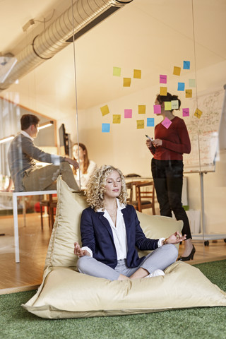 Woman doing yoga in bean bag with meeting in background stock photo