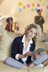 Porträt einer Frau im Büro, die ein Tablet in einem Sitzsack benutzt, mit einem Treffen im Hintergrund - PESF00684