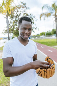 Porträt eines lächelnden jungen Mannes mit Ball und Baseballhandschuh - KIJF01555