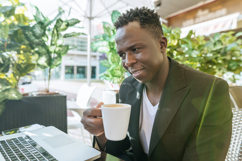 Geschäftsmann sitzt mit Laptop in einem Straßencafé und trinkt Kaffee, lizenzfreies Stockfoto