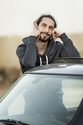 Portrait of daydreaming young man leaning on roof of his car - DMOF00012