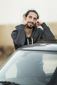 Porträt eines träumenden jungen Mannes, der sich auf das Dach seines Autos lehnt - DMOF00012
