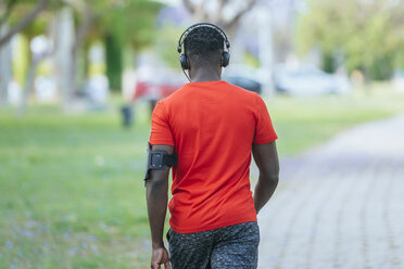 Back view of walking man in sportswear listening music with headphones - KIJF01565