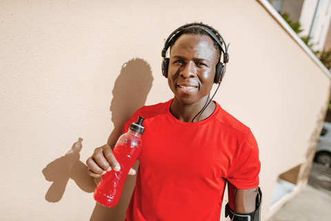 Porträt eines Mannes mit isotonischem Getränk in Sportkleidung, der mit Kopfhörern Musik hört, lizenzfreies Stockfoto