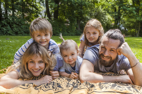 Porträt einer glücklichen Familie auf einer Wiese liegend - TCF05435