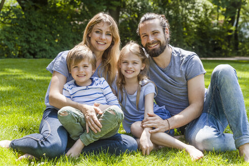 Porträt einer glücklichen Familie auf einer Wiese sitzend - TCF05439