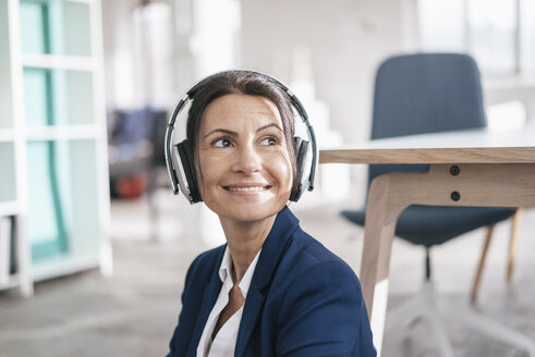 Porträt einer lächelnden Geschäftsfrau in einem Loft, die mit Kopfhörern Musik hört - JOSF01165