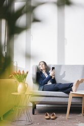 Geschäftsfrau sitzt auf einer Couch in einem Loft und schaut aus dem Fenster - JOSF01170