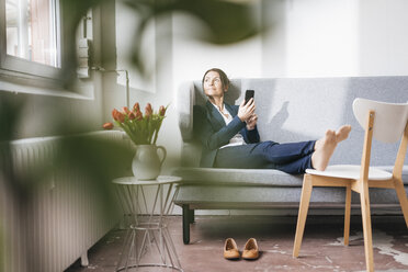 Geschäftsfrau sitzt auf einer Couch in einem Loft und schaut aus dem Fenster - JOSF01171