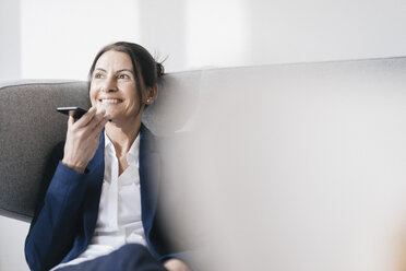 Portrait of smiling businesswoman sitting on couch using cell phone - JOSF01173