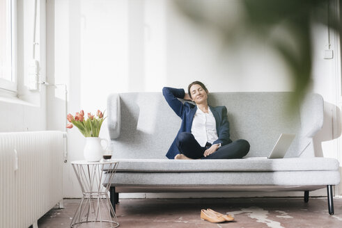 Geschäftsfrau entspannt sich auf einer Couch in einem Loft - JOSF01176