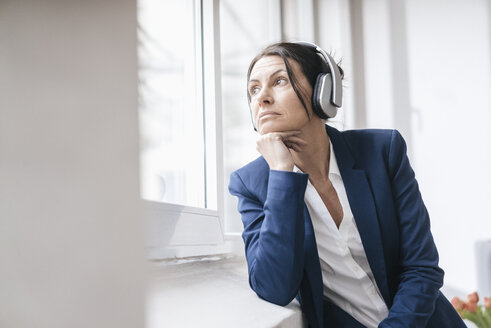Porträt einer Frau, die aus dem Fenster schaut, während sie mit Kopfhörern Musik hört - JOSF01178