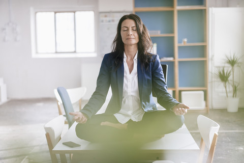 Geschäftsfrau macht Yoga-Übungen auf dem Schreibtisch in einem Loft, lizenzfreies Stockfoto