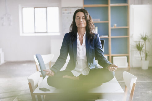 Geschäftsfrau macht Yoga-Übungen auf dem Schreibtisch in einem Loft - JOSF01182