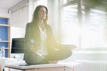 Businesswoman doing yoga exercise on desk in a loft - JOSF01183