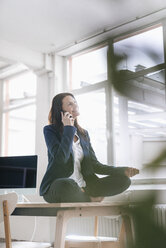 Geschäftsfrau am Telefon macht Yoga-Übungen auf dem Schreibtisch in einem Loft - JOSF01184