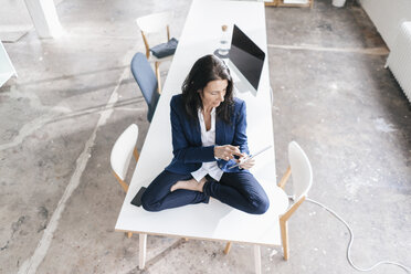 Geschäftsfrau sitzt am Schreibtisch in einem Loft und benutzt ein Tablet - JOSF01186
