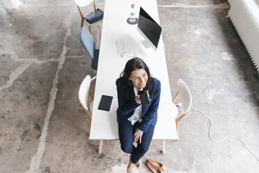 Lächelnde Geschäftsfrau auf einem Schreibtisch in einem Loft sitzend - JOSF01190