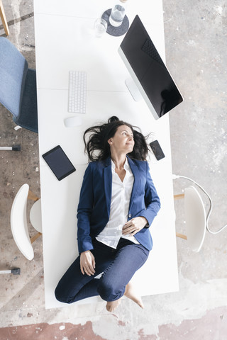 Geschäftsfrau liegend auf dem Schreibtisch im Büro, lizenzfreies Stockfoto