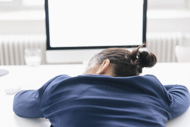 Rückenansicht einer überarbeiteten Frau, die auf dem Schreibtisch im Büro schläft - JOSF01213