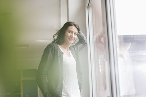 Porträt einer lächelnden Frau, die neben einem Fenster in einem Loft steht, lizenzfreies Stockfoto
