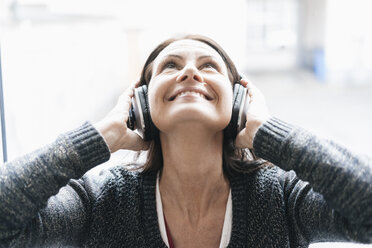 Porträt einer lächelnden Frau, die mit Kopfhörern Musik hört und nach oben schaut - JOSF01226