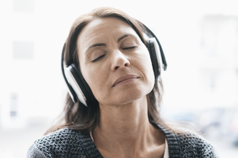 Porträt einer Frau mit geschlossenen Augen, die mit Kopfhörern Musik hört, lizenzfreies Stockfoto