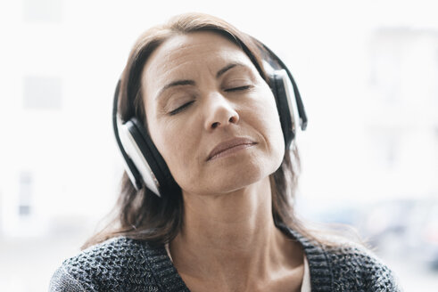 Porträt einer Frau mit geschlossenen Augen, die mit Kopfhörern Musik hört - JOSF01227