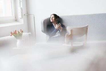 Businesswoman sitting on couch in a loft looking out of the window - JOSF01234