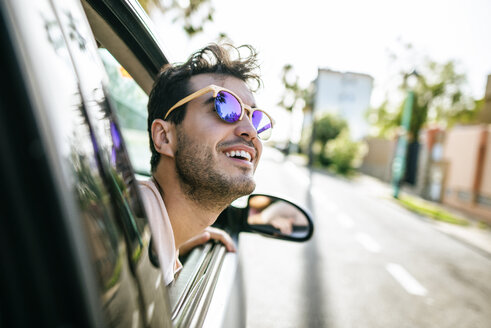 Mann mit Sonnenbrille lehnt sich aus dem Fenster eines fahrenden Autos - KIJF01588