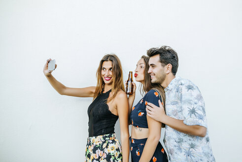Freunde machen ein Selfie mit Smartphone vor einer weißen Wand - KIJF01620