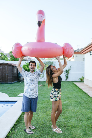 Paar hält rosa Flamingo Schwimmer am Rande des Pools, lizenzfreies Stockfoto