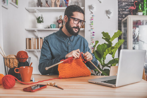 Bärtiger Mann, der zu Hause strickt und dabei seinen Laptop benutzt, um sich ein Online-Tutorial anzusehen - RTBF00902