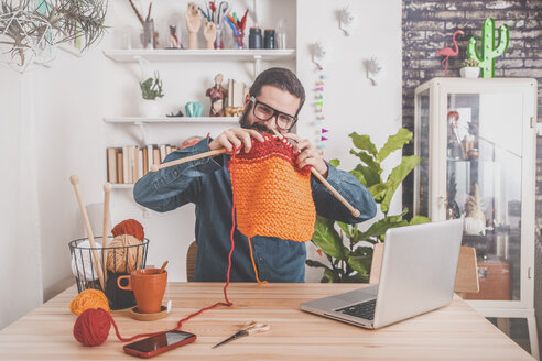 Bärtiger Mann, der zu Hause strickt und dabei seinen Laptop benutzt, um sich ein Online-Tutorial anzusehen - RTBF00904