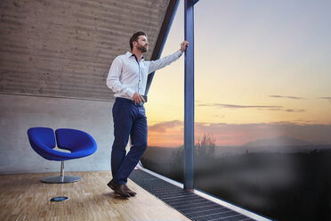 Geschäftsmann in einem Büro im Dachgeschoss, der bei Sonnenuntergang aus dem Fenster schaut - RHF01939