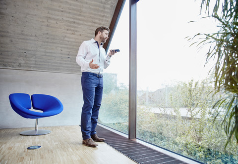 Geschäftsmann mit Handy im Dachgeschoss Büro am Fenster, lizenzfreies Stockfoto