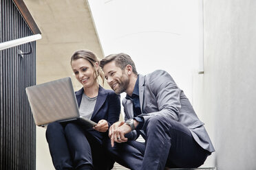 Businessman and businesswoman sitting on stairs in office sharing laptop - RHF01961